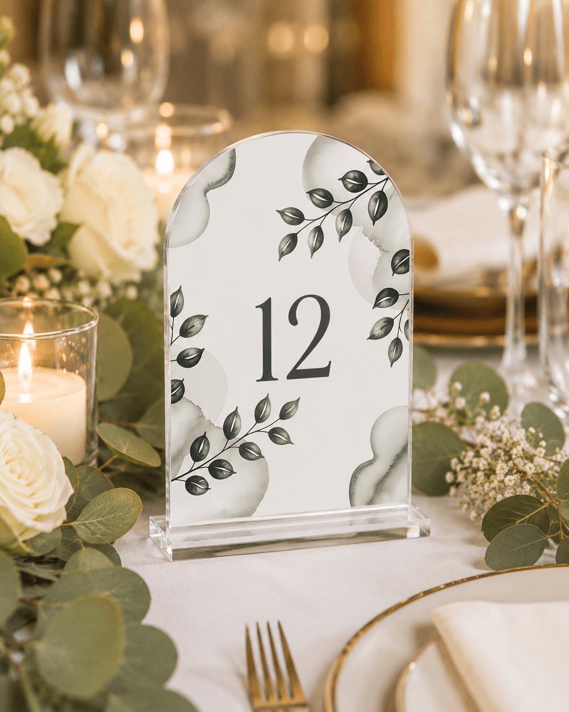 A printed acrylic table number on a set wedding table with candles and greenery